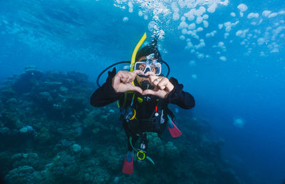 A woman is underwater with his hands together, making a heart shape. 