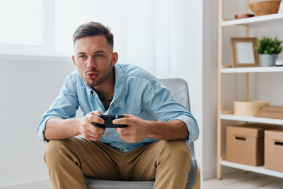 Portrait of young man using mobile phone while sitting at home