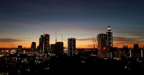 Illuminated buildings in city against sky during sunset