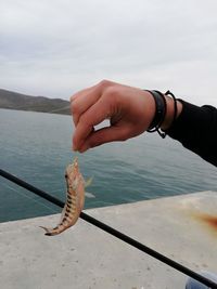 Midsection of man fishing at sea against sky