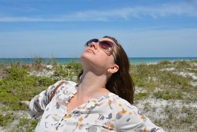 Young woman wearing sunglasses on beach against sky