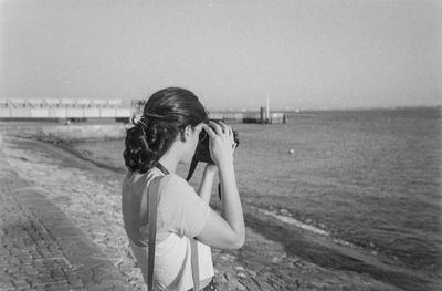 Woman holding umbrella while standing on beach against sky