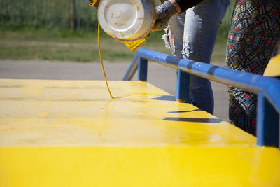 Midsection of woman pouring paint on wall outdoors