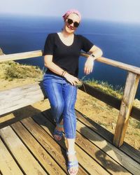 Young woman wearing sunglasses standing by sea against sky