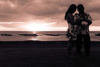 Silhouette couple standing on beach against sky during sunset