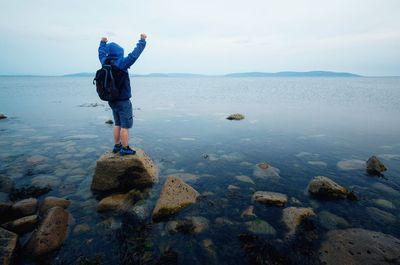 Rear view of man standing on rock by sea against sky