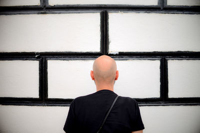 Rear view of man in black standing against black and white wall