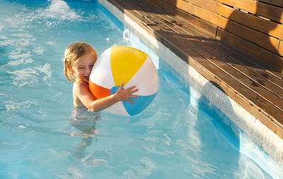 High angle view of happy kid in swimming in pool with ball