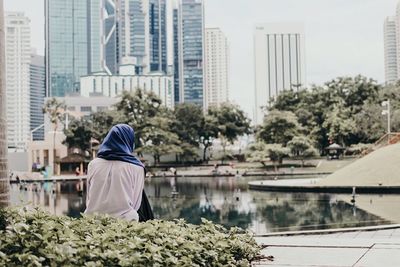 Rear view of woman sitting at lakeshore in city