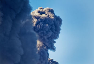 Low angle view of smoke emitting from volcanic against blue sky