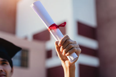 Cropped hand of man holding diploma outdoors