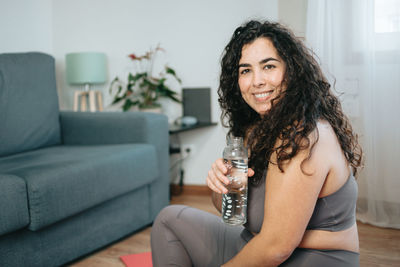 Portrait of young woman holding water bottle at home