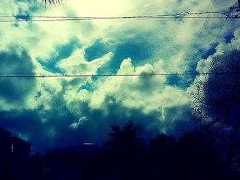 Low angle view of electricity pylon against cloudy sky