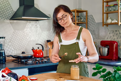Woman making healthy breakfast or brunch, spreading peanut butter on a puffed corn cakes. 