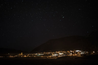 Illuminated town by mountain against star field