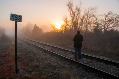Rear view of man standing by railroad tracks against sky