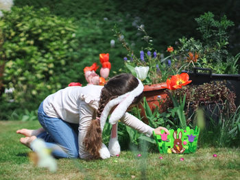 Caucasian girl with bunny ears rim collects chocolate easter eggs on the lawn.