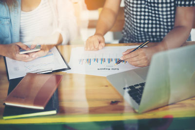 Midsection of woman with colleague writing on chart seen through glass