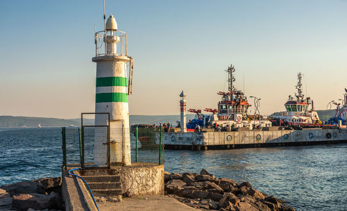 Lighthouse on pier by sea against clear sky