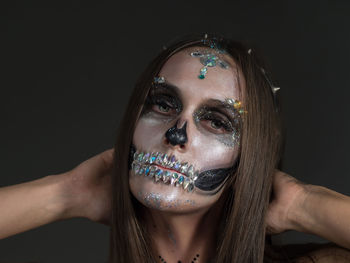 Close-up portrait of young woman with spooky face paint against black background