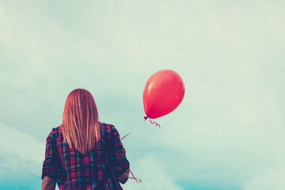 Rear view of woman with red balloon standing against cloudy sky