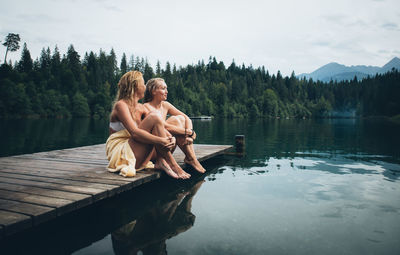 Woman sitting by lake against sky