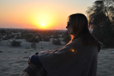 Woman covered in blanket sitting on beach at sunset during winter