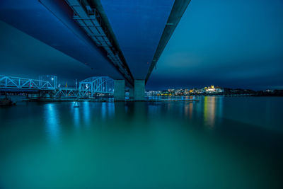 Illuminated bridge over sea against sky at night