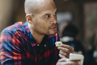 Mid adult man having food while holding mobile phone in coffee shop