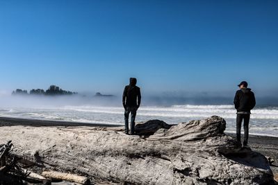 Rear view of men standing on rock against sea