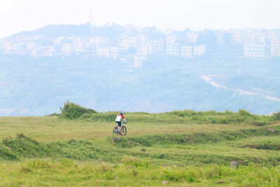 Man riding bicycle on field against sky