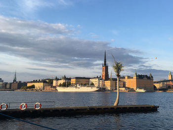 View of buildings by river against cloudy sky