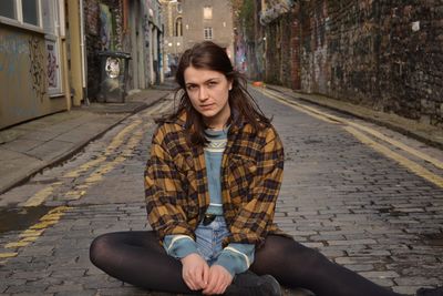Portrait of beautiful young woman sitting on street
