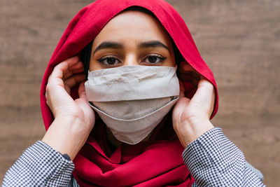 Calm arab female in hijab standing in street and putting on protective mask during coronavirus epidemic while looking at camera