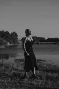 Woman standing on field by lake against sky