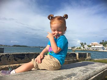 Cute smiling girl sitting on bench by sea