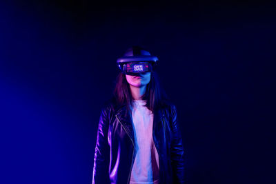 Unrecognizable female wearing modern headset with game over inscription while exploring virtual reality in dark room with neon light near wall