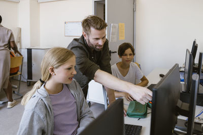 Male teacher pointing at monitor while explaining female student in classroom at school