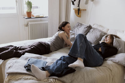 Happy female friends having fun while lying on bed in apartment