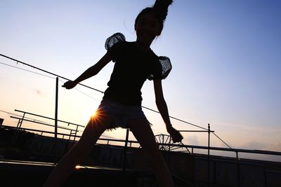 Low angle view of silhouette girl standing against clear sky during sunset