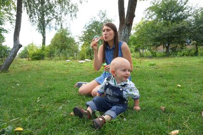 Playful baby boy with mother blowing bubbles in back yard