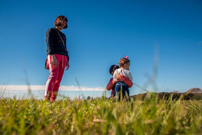 Surface level of mother with children on grassy land against blue sky