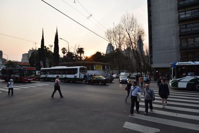 People on street in city against sky at sunset