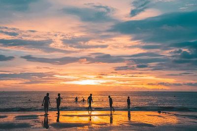 Silhouette people at beach against cloudy sky during sunset