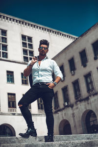 Full length portrait of man standing against building in city during sunny day