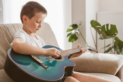 Adorable little boy learning to play acoustic guitar at home. hobbies and entertainment for children