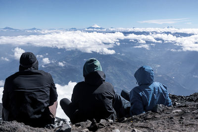 Rear view of male friends sitting on mountain against sky