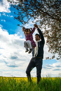 Father and daughter playing while standing on field against sky