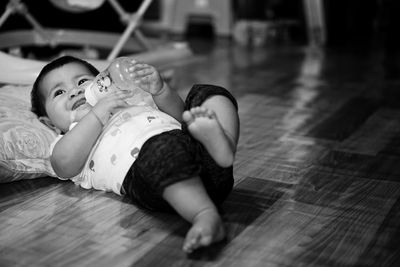Full length of toddler with milk bottle lying on floor at home