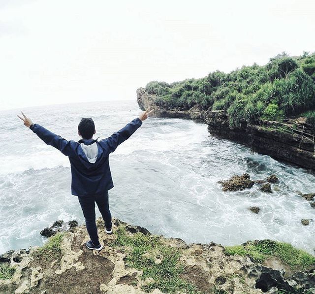 water, lifestyles, full length, leisure activity, standing, rear view, rock - object, sea, casual clothing, men, scenics, nature, beauty in nature, tranquility, tranquil scene, sky, vacations, horizon over water